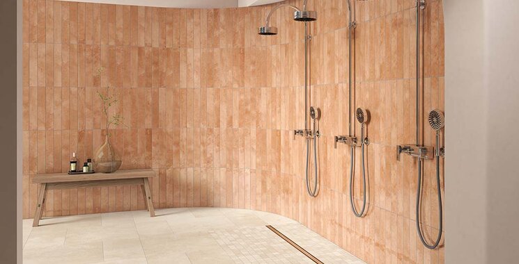 Cottofarbene Wandfliesen im länglichen Format mit matter und glänzender Struktur in einer offenen Dusche mit drei Brausen.