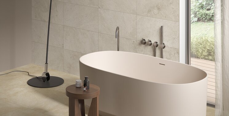 Großformatige Boden- und Wandfliesen in warmer Natursteinoptik neben freistehender Badewanne