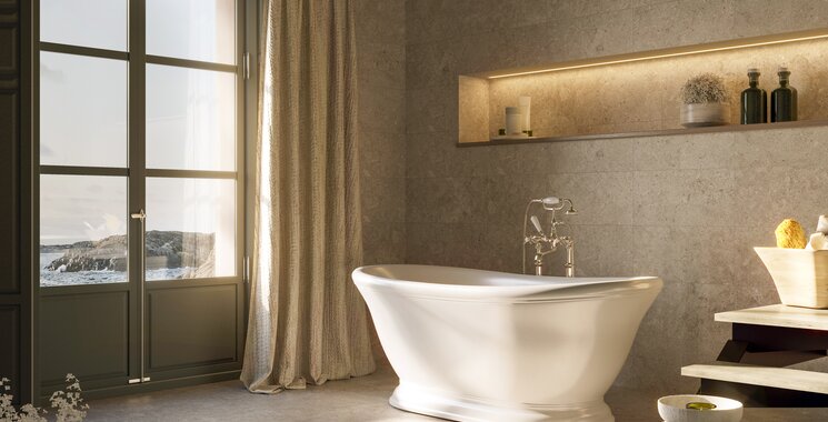 Badezimmer mit graubeigen Fliesen in Natursteinoptik an Wand und Boden und freistehender Badewanne